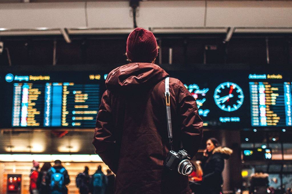 A man in a red coat is checking the airport board.